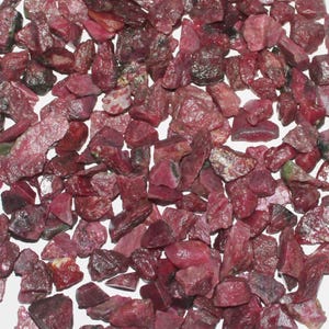 Puede incluir: Un montón de pequeñas piedras preciosas de rubí rojo sin pulir. Los rubíes son de varias formas y tamaños, algunos tienen un tono rojo más oscuro que otros.