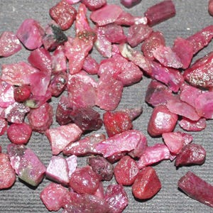 May include: A collection of loose ruby gemstones in various shapes and sizes. The rubies are a deep red color and have a natural, unpolished finish.