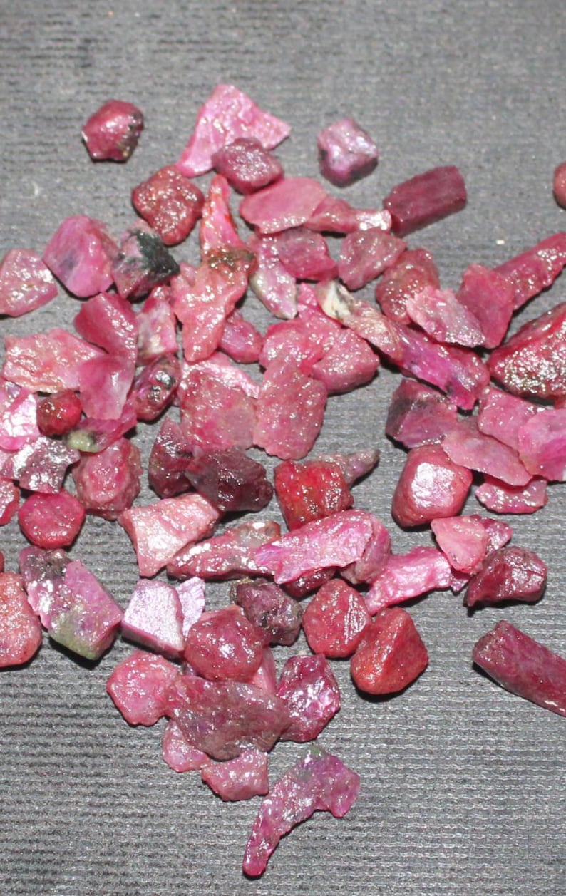 May include: A collection of loose ruby gemstones in various shapes and sizes. The rubies are a deep red color and have a natural, unpolished finish.