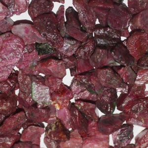 Op de afbeelding: Een close-up van een stapel ruwe, roze robijn edelstenen. De stenen zijn van verschillende groottes en vormen, sommige vertonen een donkerdere, bijna zwarte kleur.