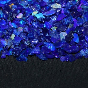 May include: A close-up of a pile of blue opal gemstones. The opals are various sizes and shapes, and they have a iridescent sheen.