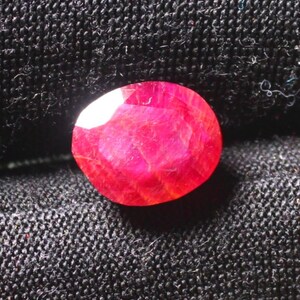 Puede incluir: Una piedra preciosa de rub&iacute; rojo intenso con un corte facetado. El rub&iacute; est&aacute; colocado sobre un fondo de tela negra.