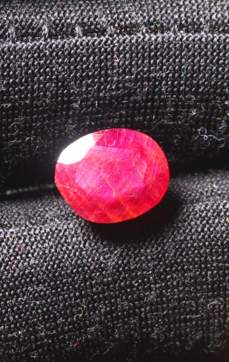 Puede incluir: Una piedra preciosa de rub&iacute; rojo intenso con un corte facetado. El rub&iacute; est&aacute; colocado sobre un fondo de tela negra.