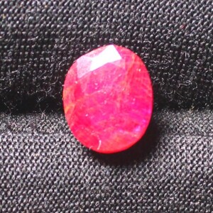 Puede incluir: Una gema ovalada de color rojo vibrante con un corte facetado. La gema tiene una apariencia ligeramente transl&uacute;cida con inclusiones visibles.