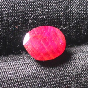 Puede incluir: Una piedra preciosa ovalada de color rojo intenso con una textura ligeramente rugosa.