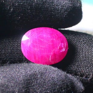 K&ouml;nnte beinhalten: Ein leuchtend rosa ovaler Edelstein mit einer glatten, polierten Oberfl&auml;che. Der Edelstein hat ein subtiles, gestreiftes Muster.