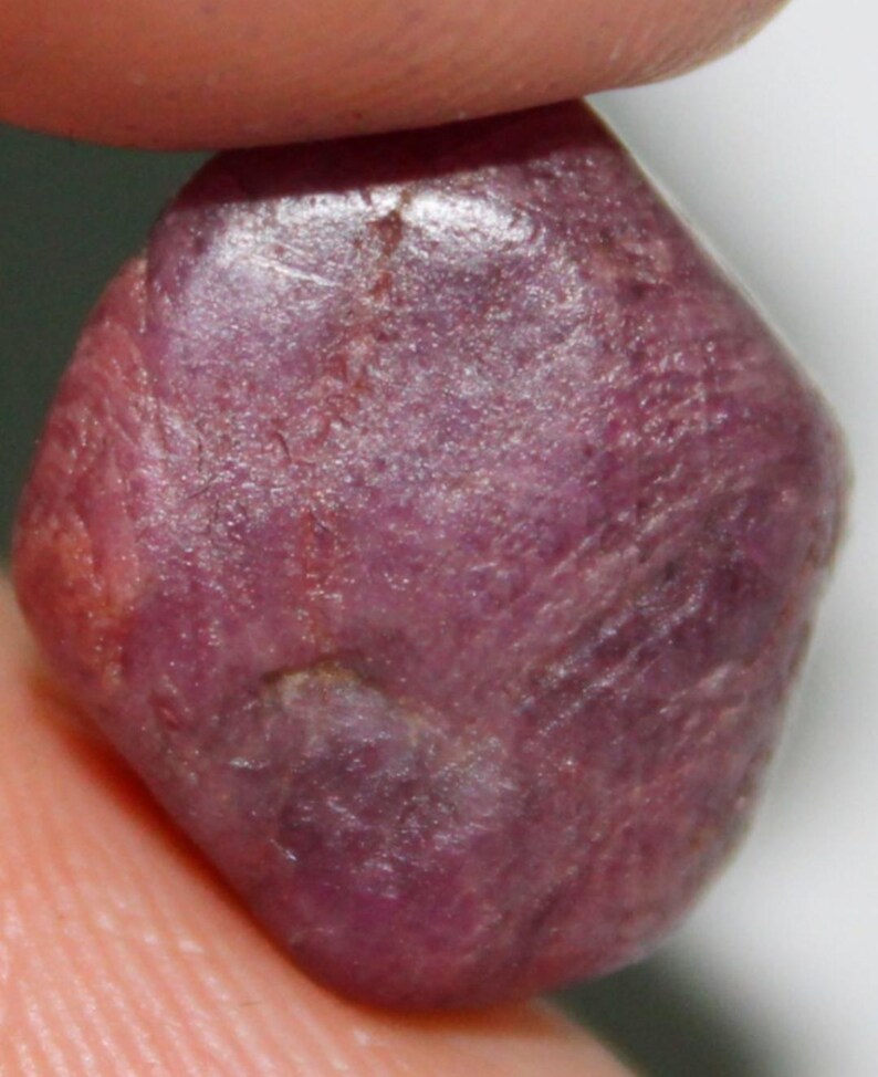 Op de afbeelding: Een diep roze, ruw geslepen edelsteen met een licht onregelmatige vorm.