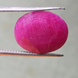 K&ouml;nnte beinhalten: Ein leuchtend rosa ovaler Edelstein, wahrscheinlich ein Rubin, wird von einer Pinzette gehalten.