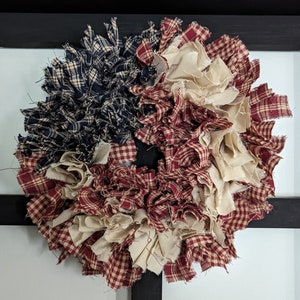 May include: A patriotic wreath made from red, white and blue fabric scraps. The wreath is made of a variety of fabrics, including plaid and gingham. The wreath is perfect for decorating for the Fourth of July or other patriotic holidays.