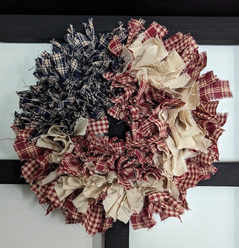 May include: A patriotic wreath made from red, white and blue fabric scraps. The wreath is made of a variety of fabrics, including plaid and gingham. The wreath is perfect for decorating for the Fourth of July or other patriotic holidays.
