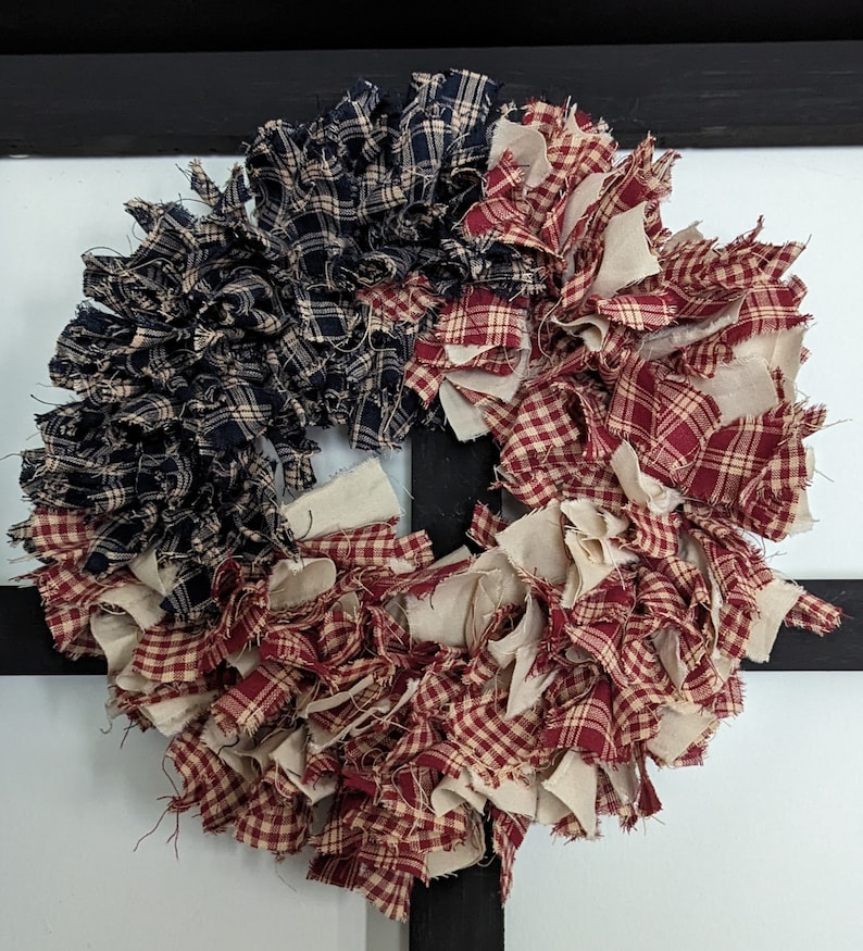 May include: A red, white and blue fabric wreath with a gingham pattern. The wreath is made of fabric scraps and is perfect for a patriotic display.