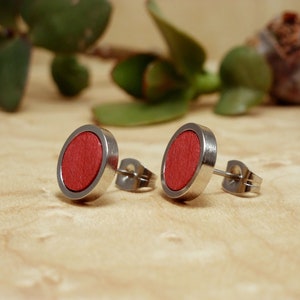 Könnte beinhalten: Ein Paar silberne Ohrstecker mit roten Holzeinlagen. Die Ohrringe sind rund und liegen auf einer Holzoberfläche.