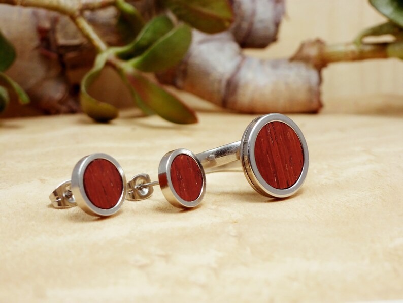 May include: Three pairs of stainless steel earrings with red wood inlay. The earrings are in different sizes.