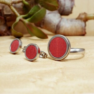 May include: A set of three jewelry pieces featuring a red wood inlay. The set includes a ring and two stud earrings.