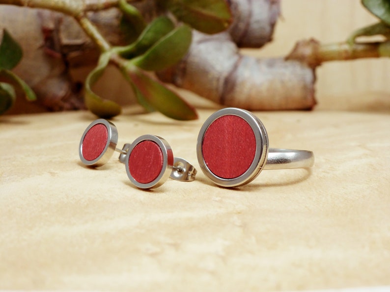 May include: A set of three jewelry pieces featuring a red wood inlay. The set includes a ring and two stud earrings.