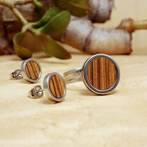 May include: A set of wooden jewelry featuring a ring and a pair of earrings. The ring and earrings have a silver band with a round wooden inlay.