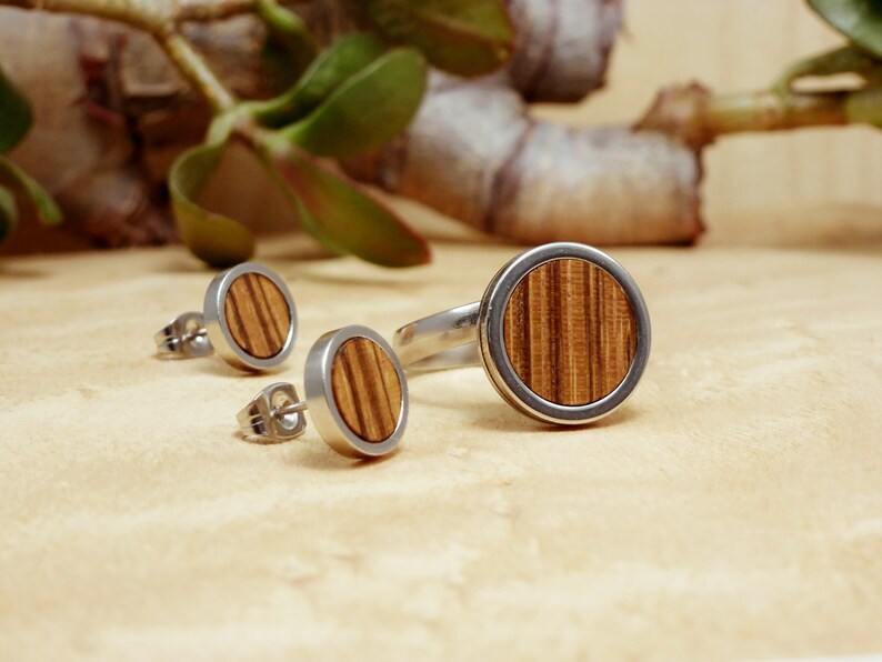 May include: A set of wooden jewelry featuring a ring and a pair of earrings. The ring and earrings have a silver band with a round wooden inlay.