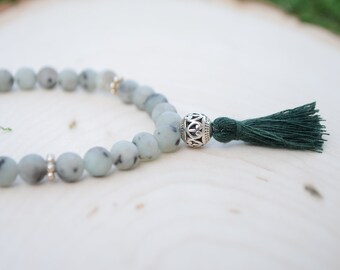 May include: A green and white beaded bracelet with a silver charm and a green tassel.