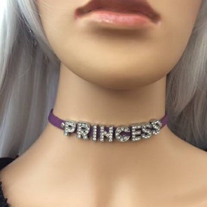 May include: Purple choker necklace with the word "PRINCESS" spelled out in silver letters with rhinestones.