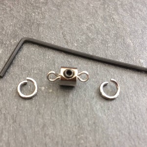 May include: A silver magnetic clasp with two silver jump rings and a black allen wrench.
