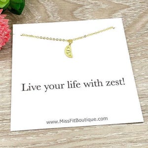 May include: A gold-colored necklace with a lemon slice pendant is displayed on a white card. The card has the text "Live your life with zest!" and the website address www.MissFitBoutique.com.