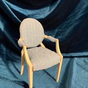 Puede incluir: Un sillón azul claro con un patrón floral en la tela. El sillón tiene un respaldo redondeado y patas de madera.