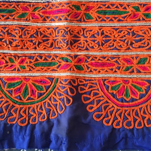 May include: A close-up of a blue fabric with intricate embroidery in orange, green, and pink. The embroidery features floral and geometric patterns.