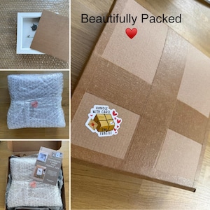 May include: A package prepared for shipping, showing a framed artwork, bubble wrap, and a cardboard box. The box is sealed with tape and features a sticker that says "Handle with Care! I'm Fragile."