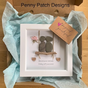 May include: A framed artwork featuring a couple on a swing, crafted from stones and driftwood. The white frame holds a scene with a small bouquet, two heart-shaped wooden accents with the word "Love", and a card that says "beyond grateful". The text "Penny Patch Designs" is visible.