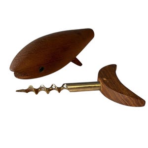 May include: A wooden corkscrew shaped like a fish. The corkscrew is made of dark brown wood and has a metal spiral. The fish is in a horizontal position with its tail pointing to the right.