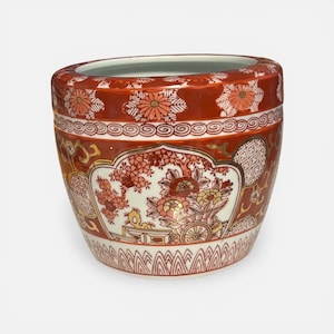 May include: A ceramic planter with a wide, rounded shape. The planter is primarily red with floral and geometric patterns in white, orange, and gold. The design includes a central cart and floral arrangement. The planter's rim has a repeating floral pattern.