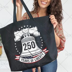 Puede incluir: Bolso tote negro con un gr&aacute;fico blanco desgastado de la Campana de la Libertad, el n&uacute;mero 250 y el texto "YEARS OF LIBERTY" en una pancarta roja, blanca y azul. El dise&ntilde;o est&aacute; rodeado de estrellas.