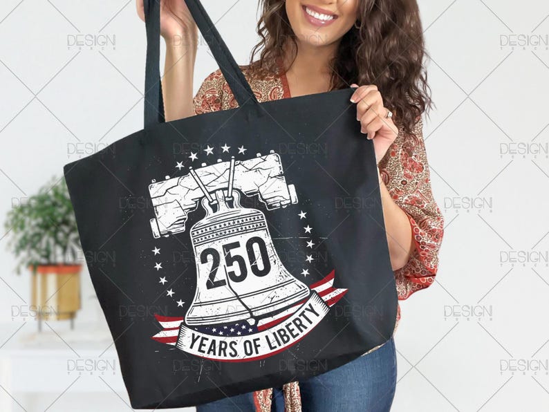 Puede incluir: Bolso tote negro con un gr&aacute;fico blanco desgastado de la Campana de la Libertad, el n&uacute;mero 250 y el texto "YEARS OF LIBERTY" en una pancarta roja, blanca y azul. El dise&ntilde;o est&aacute; rodeado de estrellas.