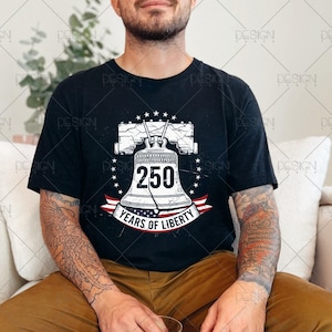 Puede incluir: Camiseta negra con un gr&aacute;fico de la Campana de la Libertad, el n&uacute;mero 250 y el texto "Years of Liberty". El dise&ntilde;o incluye estrellas y una cinta roja, blanca y azul. La camiseta la lleva una persona.