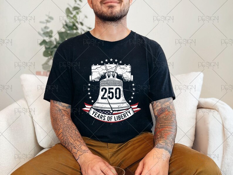 Puede incluir: Camiseta negra con un gr&aacute;fico de la Campana de la Libertad, el n&uacute;mero 250 y el texto "Years of Liberty". El dise&ntilde;o incluye estrellas y una cinta roja, blanca y azul. La camiseta la lleva una persona.