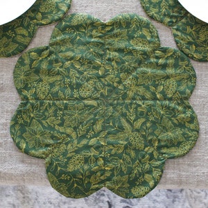 May include: A green and gold floral patterned table runner with a scalloped edge.