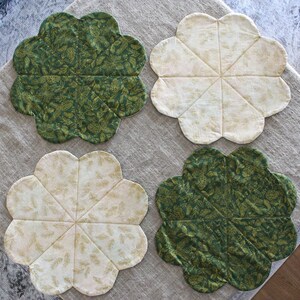 May include: Four round placemats with a scalloped edge. Two placemats are green with a gold leaf pattern and two are white with a gold leaf pattern.