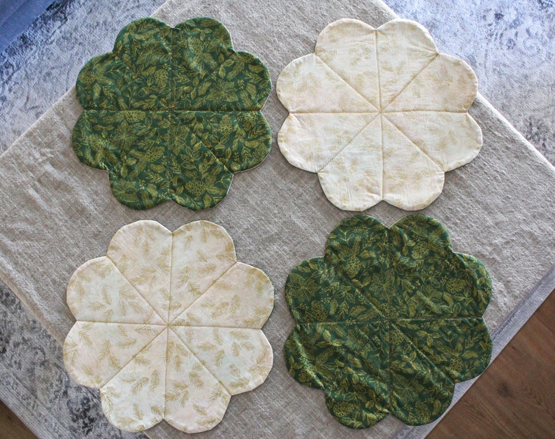 May include: Four round placemats with a scalloped edge. Two placemats are green with a gold leaf pattern and two are white with a gold leaf pattern.