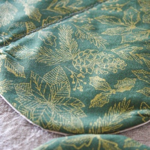 May include: Close-up of a green fabric with a gold leaf pattern. The fabric is sewn together in a curved shape, creating a unique design.