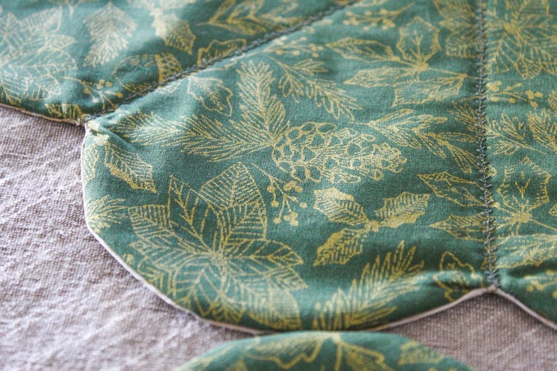 May include: Close-up of a green fabric with a gold leaf pattern. The fabric is sewn together in a curved shape, creating a unique design.