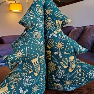 May include: A green and gold Christmas tree pillow with a festive pattern of snowflakes, holly, and ornaments. The pillow is made of fabric and is shaped like a Christmas tree.