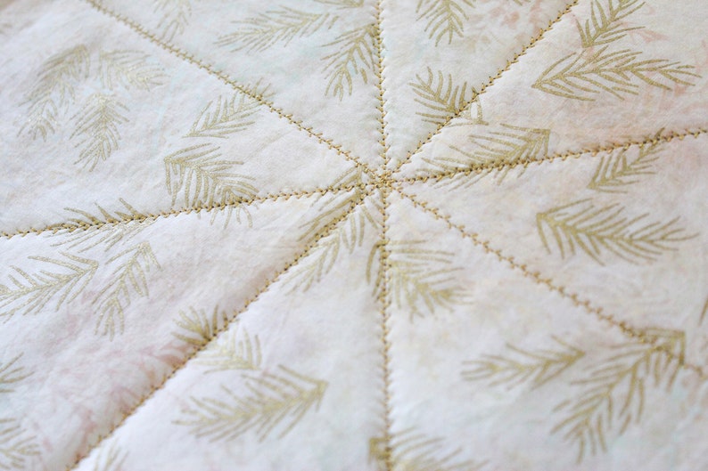 May include: A white fabric with a repeating pattern of gold pine branches. The fabric is quilted with a starburst pattern.