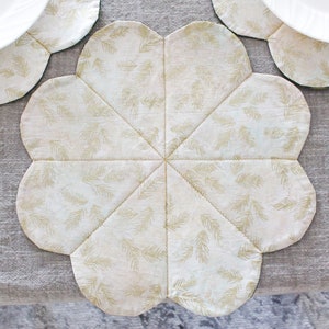 May include: A white fabric placemat with a gold leaf pattern. The placemat is shaped like a flower with six points.