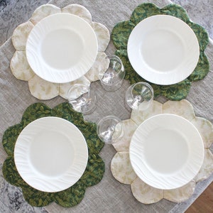 May include: Four white dinner plates with scalloped edges are placed on top of four different patterned placemats. The placemats are a combination of green and cream colors with floral designs.