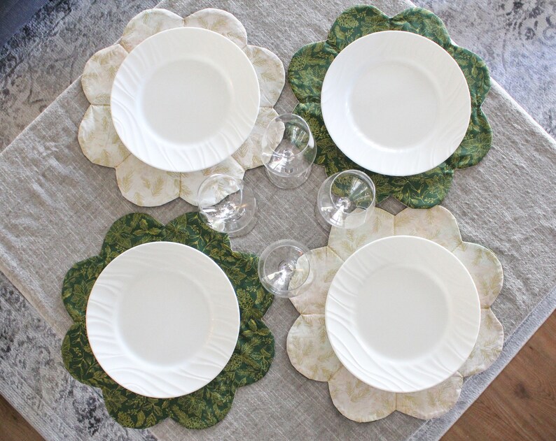 May include: Four white dinner plates with scalloped edges are placed on top of four different patterned placemats. The placemats are a combination of green and cream colors with floral designs.