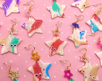 May include: A collection of 12 handmade star-shaped earrings with various colorful designs and glitter accents. Each earring features a unique pattern and color combination, including pink, blue, green, and white.