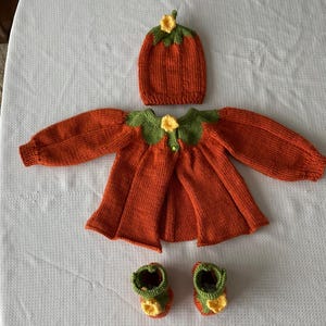 May include: A knitted pumpkin costume for a baby, including a hat, sweater, and booties. The outfit is orange with green and yellow accents.