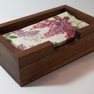 May include: A dark brown wooden napkin holder with a floral patterned napkin inside.
