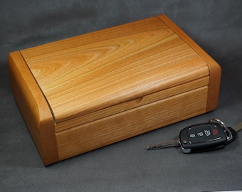 May include: A wooden box with a hinged lid, made of light brown wood with a natural wood grain. The box is closed and a car key is lying next to it.