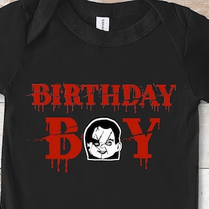 May include: Black baby onesie with a red graphic that says "Birthday Boy" with a dripping blood effect. The graphic also features a black and white illustration of a creepy doll's face.